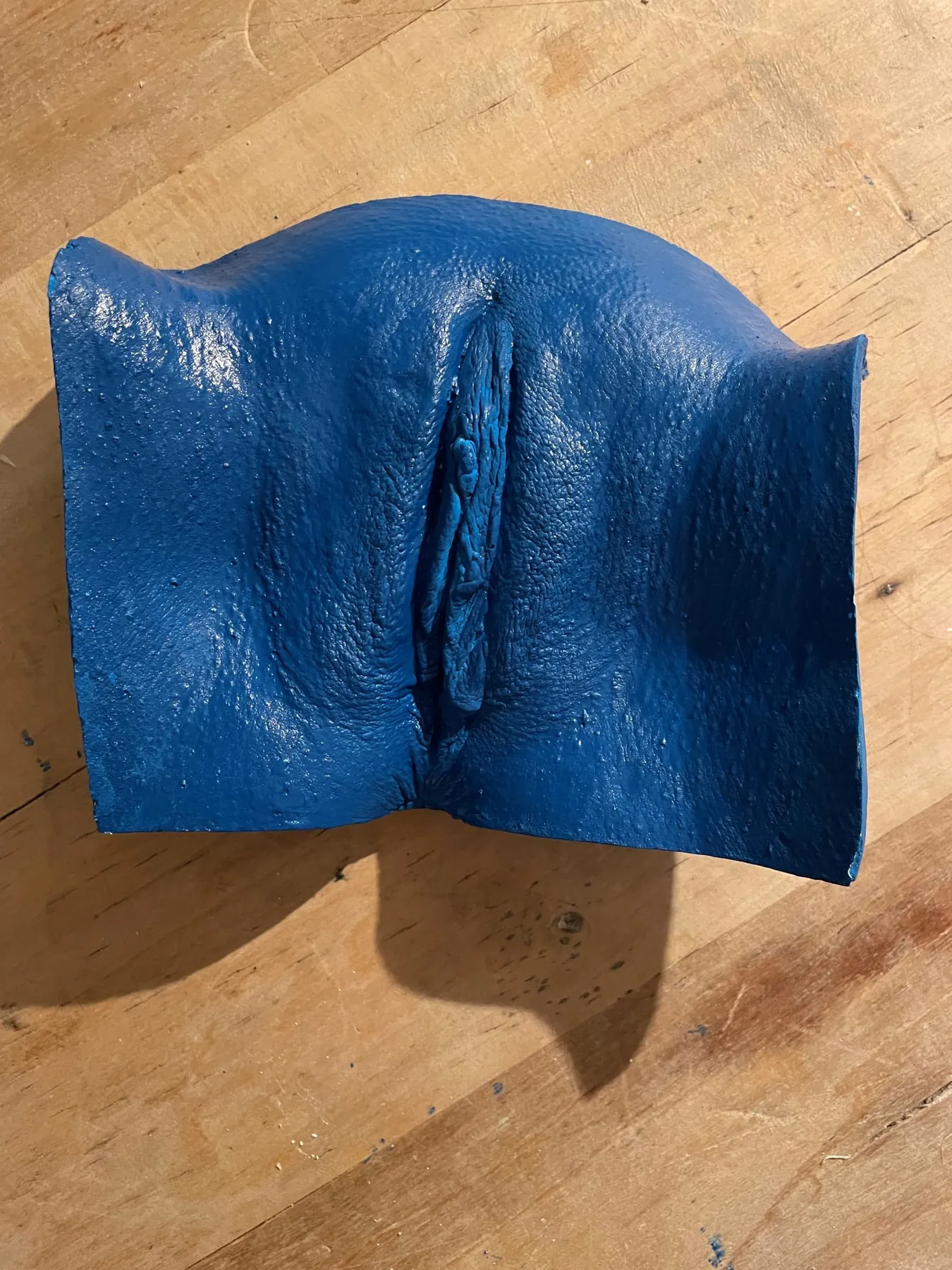 Vulva-Abformung aus tiefblau pigmentiertem Acrylharz auf einem Holztisch